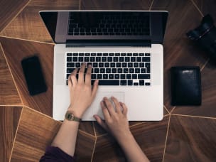 Person working on the laptop with phone, wallet and lens aside