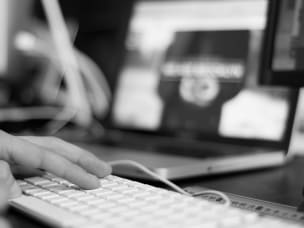 immagine in bianco e nero e mani che battono sulla tastiera di un pc