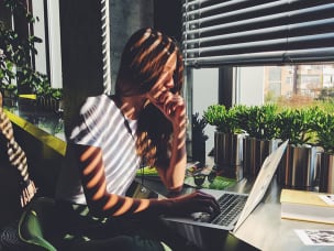 Frau sitzt mit Laptop am Fenster