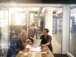 Vier Mensch stehen vor Laptop im Meetingraum