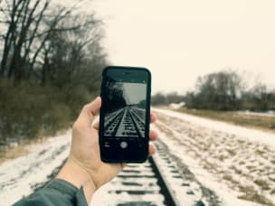 mano che impugna uno smartphone sospeso sopra dei binari innevati