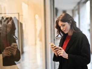 Frau steht mit Handy vor einem Schaufenster