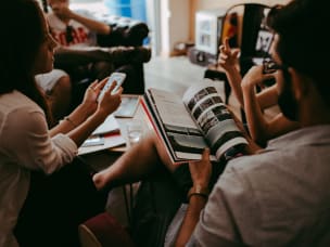 Mehrere Menschen am Tisch mit Handy und Zeitschrift