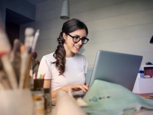 woman working from home on her laptop with paintbrushes