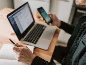 Foto di una persona al pc con in mano uno smartphone