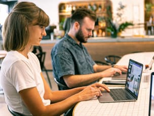 Frau und Mann sitzen mit Laptops an einem Tisch