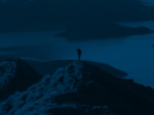 Blue-tinted transition scene with person standing on a mountain overlooking water