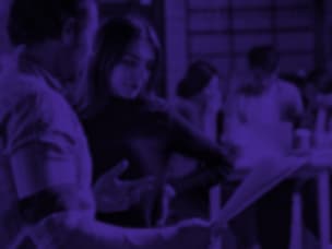 Group of people in a purple-lit room, with two individuals interacting in the foreground