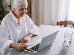 ältere Dame sitzt am Laptop und hält Kreditkarte in der Hand