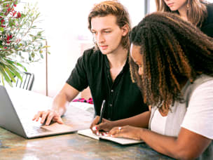 Three people collaborating at table with laptop and notebook