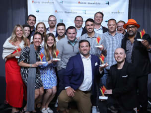 A group of seventeen people, seven of them holding awarded prizes, at the ThinkTank Network Awards