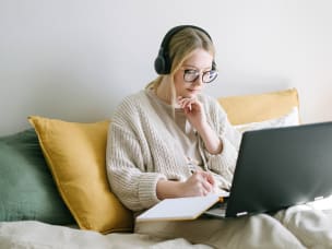 Person sitzt mit Laptop und Block auf der Couch und informiert sich über Awin's neue Vision mit dem Awin-Vorstand