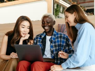 Three people sitting on a couch looking at a laptop together