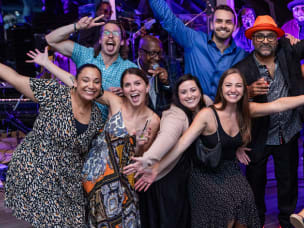 A group of eight people, including the musician, celebrating at the mThink Blue Book celebration
