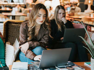 Two people working on laptops in café