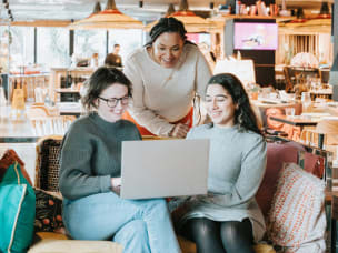 Three people viewing laptop in café