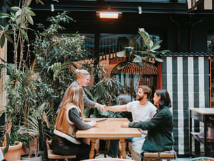 Four colleagues sitting at a table, with two of them shaking hands.  