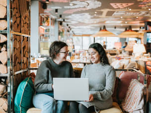 two people sitting on sofa working together on laptop