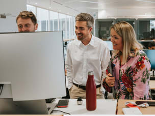 Team collaborating around a computer in an open office, illustrating workplace dynamics or digital strategy planning.