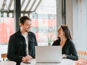 Two people at a café table looking at a laptop.