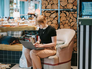 Person sitting on a cushioned chair using a laptop in a cozy setting.