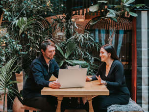 Two people discussing work at a laptop in a lush indoor setting