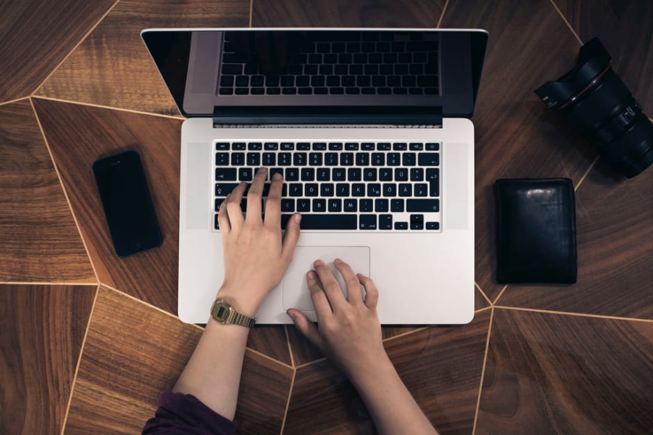 Person working on the laptop with phone, wallet and lens aside
