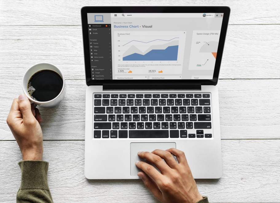 Person using laptop with business dashboard and holding a coffee cup