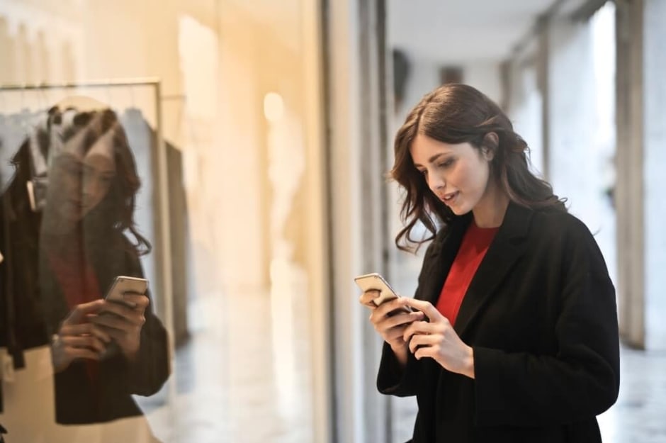 Frau steht mit Handy vor einem Schaufenster