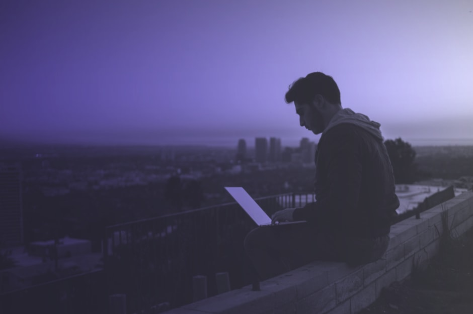 Mann sitzt mit Laptop auf einer Mauer