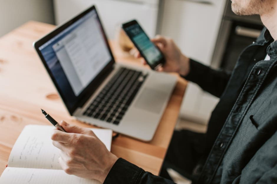 Foto di una persona al pc con in mano uno smartphone