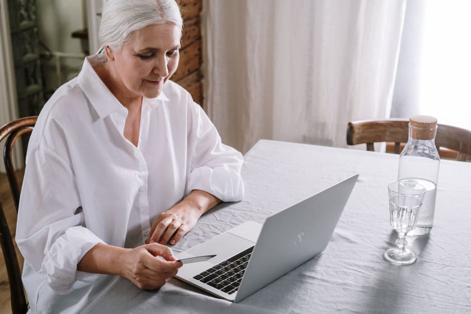 ältere Dame sitzt am Laptop und hält Kreditkarte in der Hand