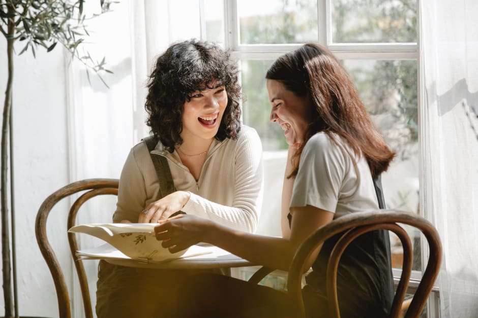Two people reading at a round table near a window with greenery