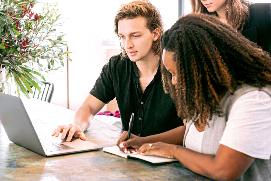 Three people collaborating at table with laptop and notebook