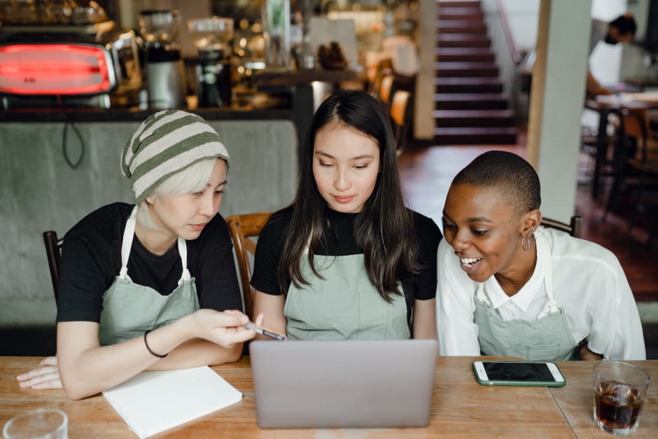 Three people in aprons viewing laptop in café