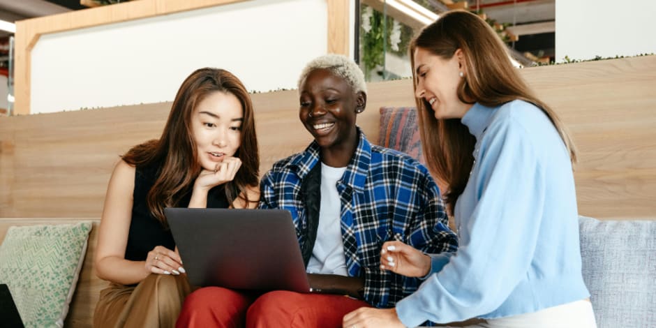 Three people sitting on a couch looking at a laptop together