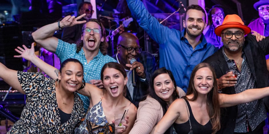 A group of eight people, including the musician, celebrating at the mThink Blue Book celebration