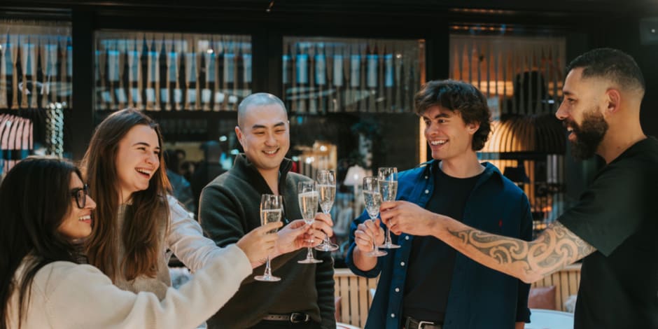 Five Awin employees raising their champagne glasses in a toast at a bar