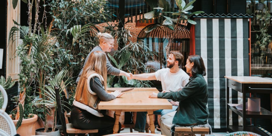 Four colleagues sitting at a table, with two of them shaking hands.  