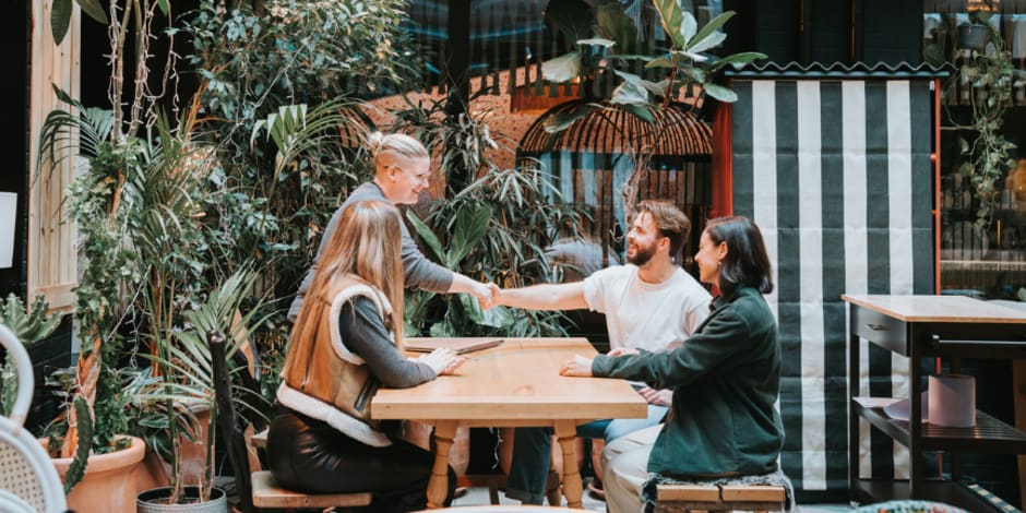 Four colleagues sitting at a table, with two of them shaking hands.  