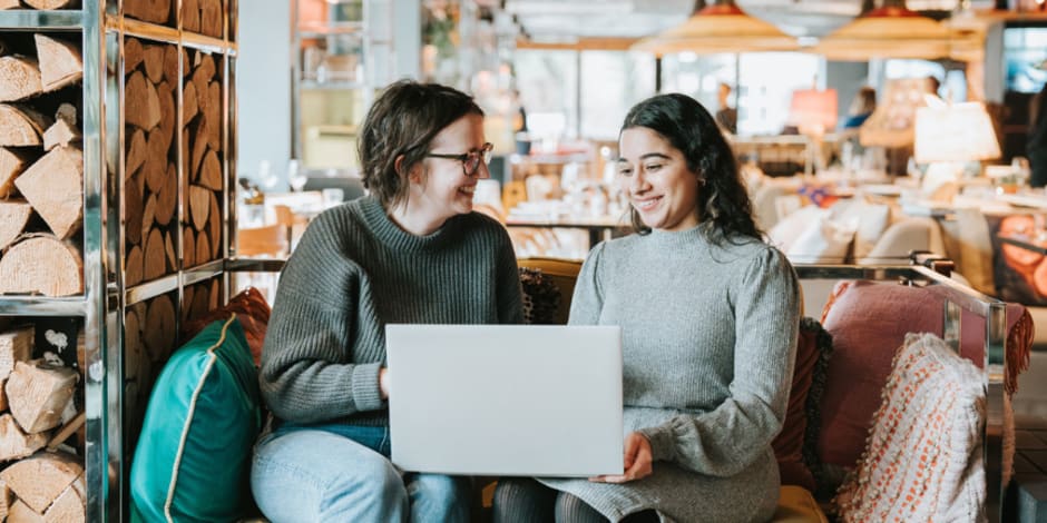 two people sitting on sofa working together on laptop