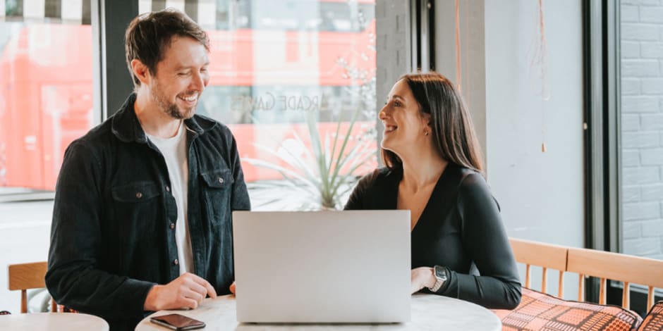 two smiley people talking in front of laptop