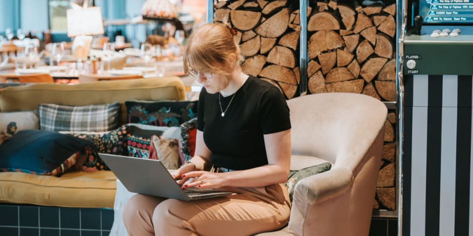 Person sitting on a cushioned chair using a laptop in a cozy setting.