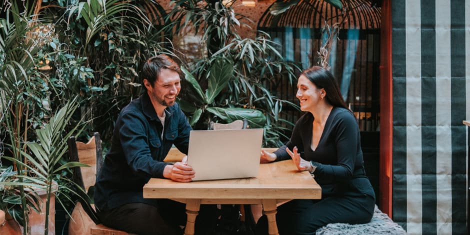 Two people discussing work at a laptop in a lush indoor setting